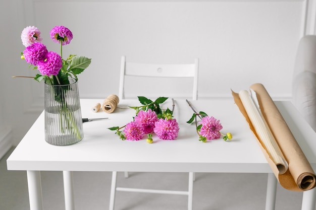 Dalie rosa e carta marrone per avvolgere i fiori giacciono su un tavolo da fiorista bianco all'interno Mockup per creare il tuo design