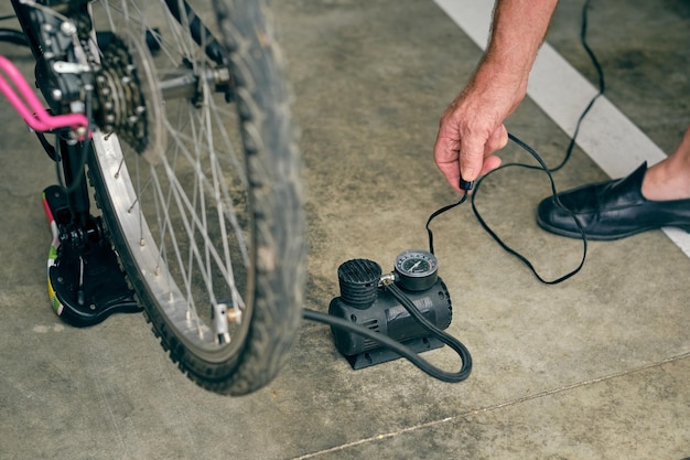 Dall'alto del raccolto bicicletta gonfiabile di gonfiaggio maschile anziano anonimo con utensile elettrico con manometro