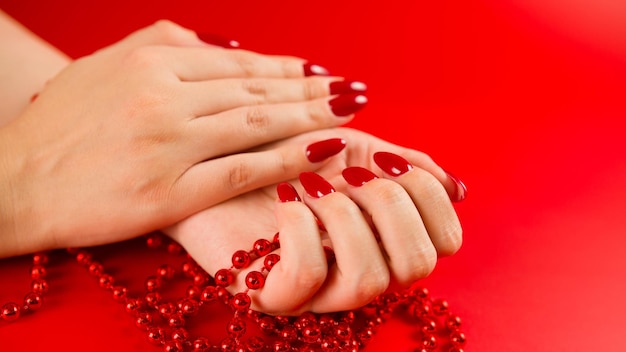 Dall'alto del raccolto donna anonima con perline rosse e con manicure rossa su sfondo rosso in studio