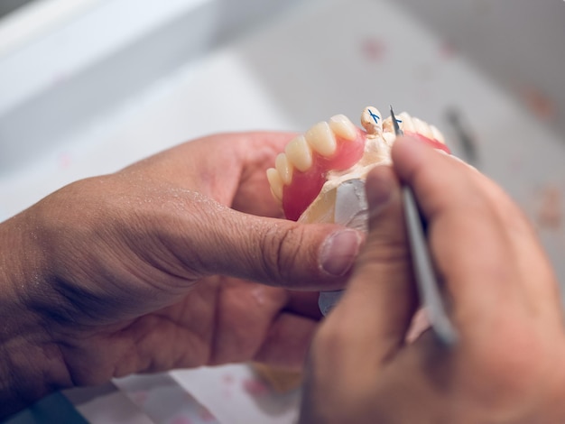 Dall'alto del raccolto specialista dentale maschio irriconoscibile che intaglia denti artificiali in ceramica utilizzando uno strumento metallico affilato mentre lavora in laboratorio odontotecnico