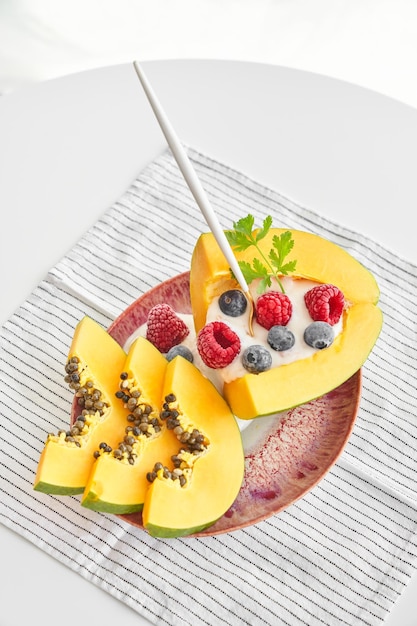 Dall'alto della porzione di dessert dolce a base di papaya, yogurt alla frutta, lamponi e mirtilli, servito su piatto con cucchiaio e adagiato su tovagliolo