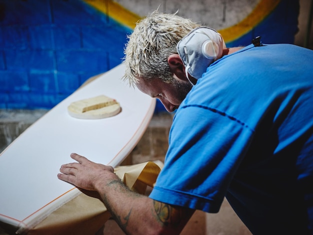 Dall'alto di concentrato shaper uomo incollare carta sul bordo della tavola da surf prima di colorare in laboratorio