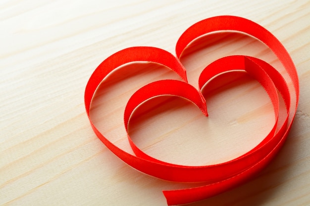 Dall'alto due nastri rossi a forma di cuore su fondo in legno.
