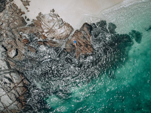Dall'alto foto di una bella giovane donna con un costume da bagno blu sdraiato sulla roccia durante l'alta marea. Concetto di vacanza estiva