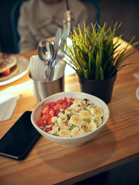 Dall'alto una ciotola di deliziosa colazione condita con fragole fresche e banane servita sul tavolo con pianta in vaso in un bar luminoso