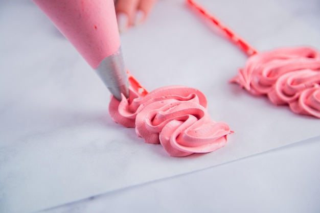 Dalla sacca da pasticcere si stende su carta da forno un bizzetto rosa con riccioli a forma di t...