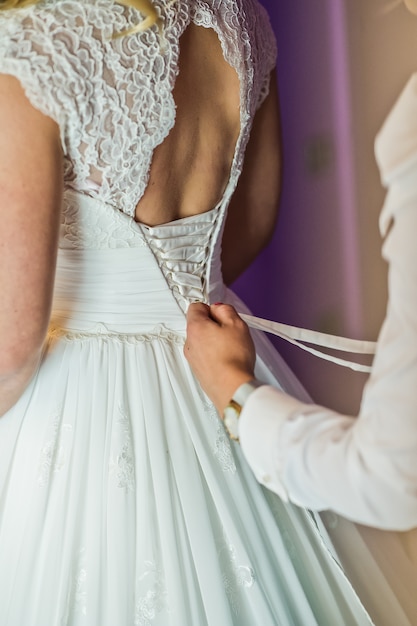 Damigella d&#39;onore aiuta a vestire la sposa abito da sposa, interni dell&#39;hotel, sfondo viola