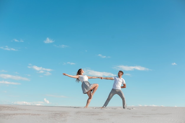 Dancing romantico delle coppie nel deserto della sabbia a cielo blu