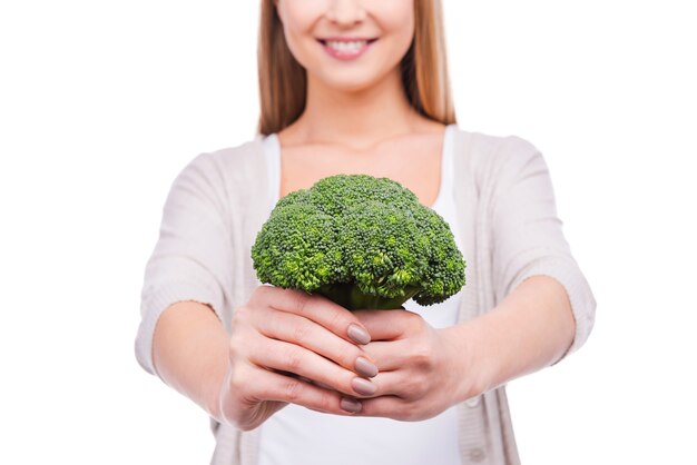 Dandoti un pozzo di vitamine. Immagine ritagliata di una bella giovane donna che allunga i broccoli e sorride mentre si trova in piedi su sfondo bianco