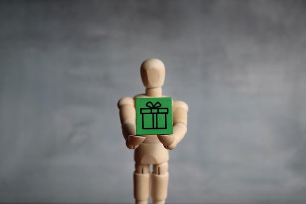 Dare il concetto di regalo presente Figura umana in legno che tiene un cubo di legno verde con l'icona della confezione regalo presente