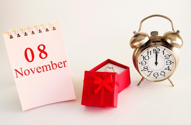 Data del calendario su sfondo chiaro con confezione regalo rossa con anello e sveglia 8 novembre