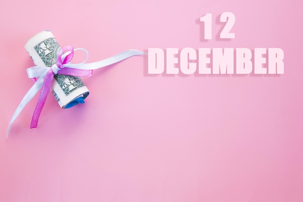 Data del calendario su sfondo rosa con banconote da un dollaro arrotolate appuntate da un nastro rosa e blu con spazio per la copia Il 12 dicembre è il dodicesimo giorno del mese