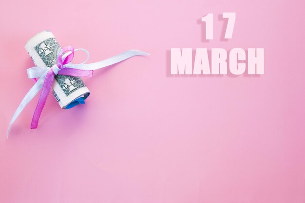 Data del calendario su sfondo rosa con banconote da un dollaro arrotolate appuntate da un nastro rosa e blu17 marzo