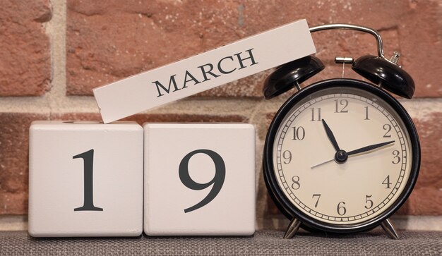 Data importante, 19 marzo, stagione primaverile. Calendario in legno sullo sfondo di un muro di mattoni. Sveglia retrò come concetto di gestione del tempo.