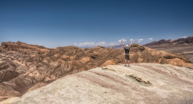 Death Valley e un felice escursionista in piedi sul bordo con le braccia alzate. Vincitore, successo e concetto di realizzazione in natura.