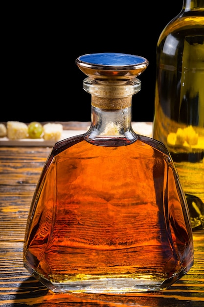 Decanter per whisky in vetro moderno ed elegante con un tappo blu e una bottiglia di vino in piedi su un tavolo di legno accanto a un buffet di formaggi sullo sfondo