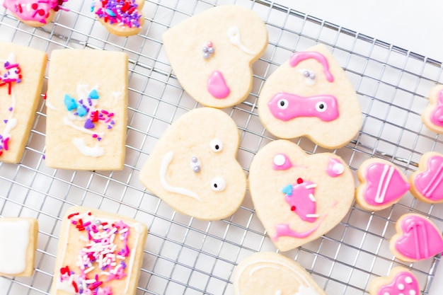 Decorare i biscotti di zucchero a forma di cuore con glassa reale e confettini rosa per San Valentino.