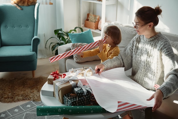 Decorare i regali di Natale famiglia madre e bambino che avvolgono insieme la confezione regalo di Natale