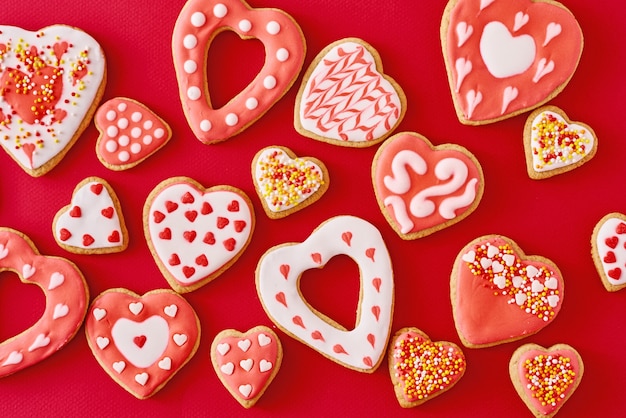 decorato con glassa e biscotti glassati a forma di cuore su superficie rossa, piatto. Concetto di cibo San Valentino