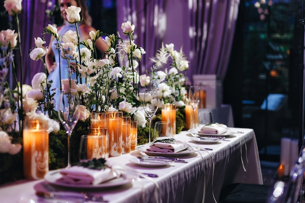 Decorazione da tavolo per matrimoni romantici con grandi mazzi floreali lussureggianti tra cui rose bianche, ranuncoli, ranuncoli persiani, orchidee bianche e candele. Foto di alta qualità