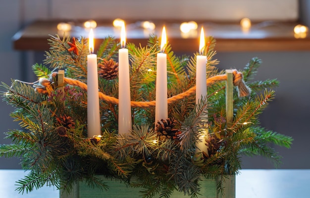 Decorazione dell'avvento con rami di abete e quattro candele accese in cesto di legno su tavolo bianco a casa