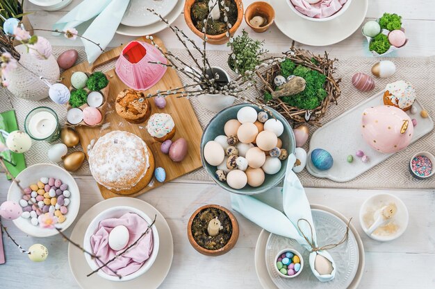 Decorazione della tavola per la celebrazione della Pasqua in cucinaTavola per le vacanze di Pasqua a casaReligiosa familiare tradizionale festiva cristianesimocibo pasto cattolicoUova di colore poptortaconiglietto divertentecaramella dolce