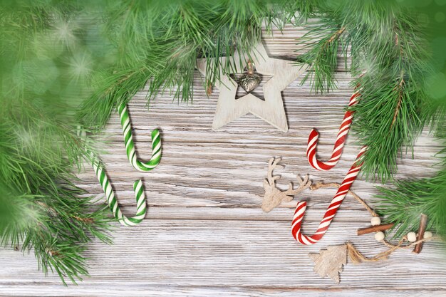 Decorazione di natale sui rami dell'albero di Natale. Bastoncini di zucchero e giocattoli di legno su fondo di legno con luce e bokeh.