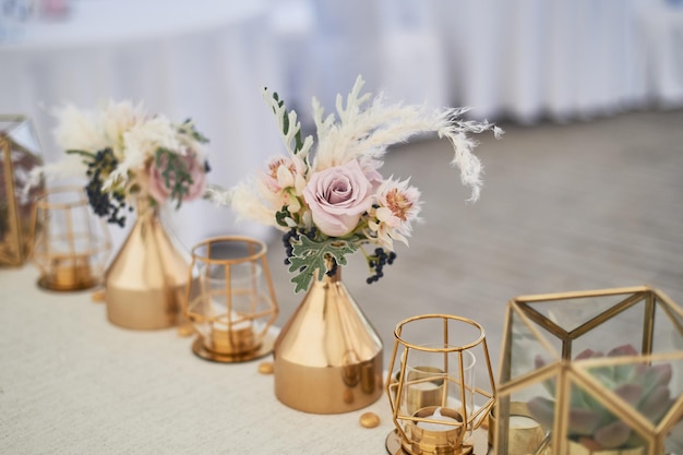 Decorazione di nozze in stile bohoColori chiari nella tenda Tavola nuziale decorata con vasi d'oro con rose e cereali E candele geometriche in candelieri d'oro