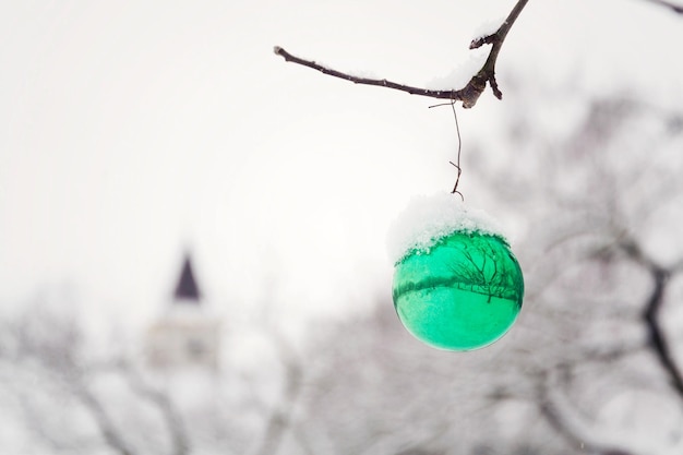 Decorazione di vetro dell'annata della palla di Natale verde che appende sull'albero all'aperto che cade sullo sfondo del paesaggio invernale della neve