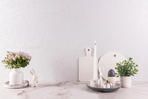 Decorazione festosa del piano di lavoro della cucina per le vacanze di Pasqua Bellissimi fiori primaverili in vasi Figurine di coniglietto di Pasqua uova che bruciano candele