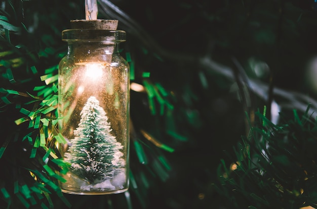 Decorazione natalizia. Appendere un piccolo albero di Natale in un barattolo di vetro su rami di pino ghirlanda di alberi di Natale e ornamenti su bokeh astratto