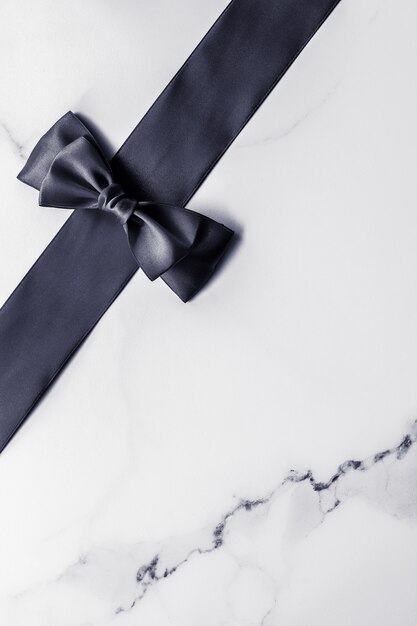 Decorazione regalo di festa e concetto di promozione della vendita nastro di seta nera e fiocco su sfondo marmo flatlay