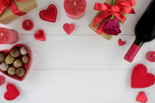 Decorazione romantica di giorno di San Valentino con rose, vino e cioccolato su un tavolo di legno bianco.