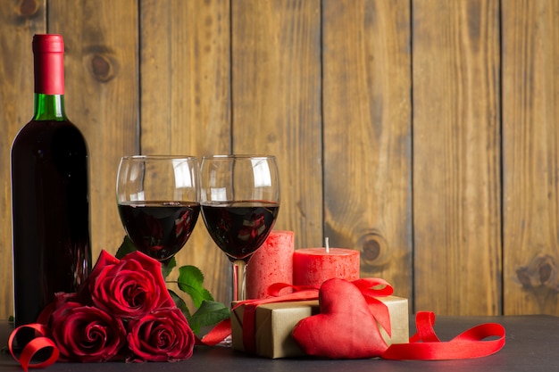 Decorazione romantica giorno di San Valentino con rose, vino e scatola regalo su un tavolo in legno marrone