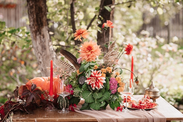 Decorazioni autunnali: bouquet di dalie, melograni, candele, zucche e bicchieri