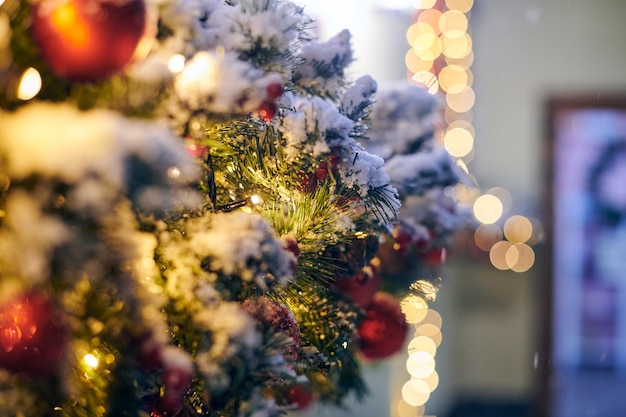 Decorazioni dell'albero di Natale con ghirlande gialle coperte di neve albero di Natale all'aperto con lampadine rosse
