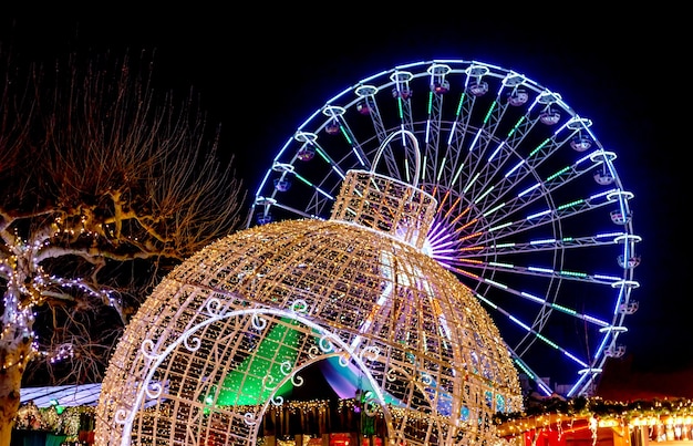 Decorazioni di Capodanno al mercatino di Natale. La ruota panoramica si illumina di notte. Palla di Natale gigante e ruota panoramica. Fiera di Natale a Maastricht, Paesi Bassi