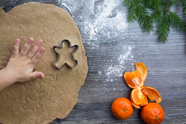 Decorazioni di Capodanno e Natale su una superficie di legno con mandarini e un albero di Natale Le mani di un bambino piccolo realizzano stampi per cuocere il pan di zenzero a forma di uomo