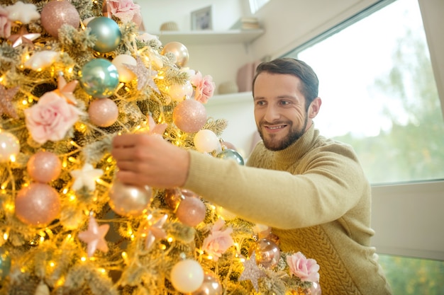 Decorazioni di Capodanno. Uomo barbuto bello che decora l'albero di nuovo anno