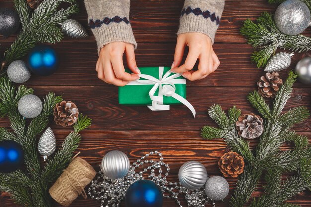 Decorazioni di Natale sul tavolo di legno con regalo decorato nelle mani di donna