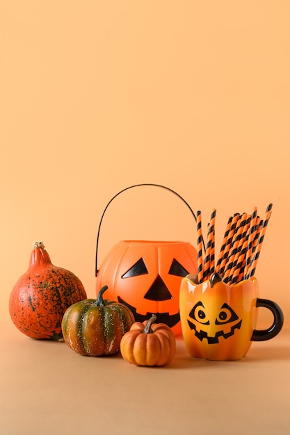 Decorazioni divertenti per feste di Halloween, ciotola di caramelle, zucche, dolci, tazza con cannuccia sull'arancia. Composizione verticale.