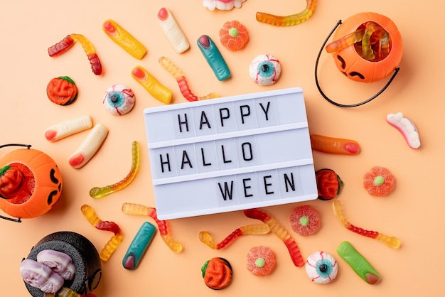 Decorazioni e dolci per le vacanze di Halloween con lightbox con parole Happy Halloween flat lay su sfondo arancione