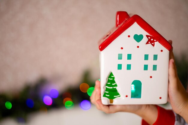 Decorazioni natalizie Casa decorativa bianca con un tetto rosso e una torcia all'interno nelle mani