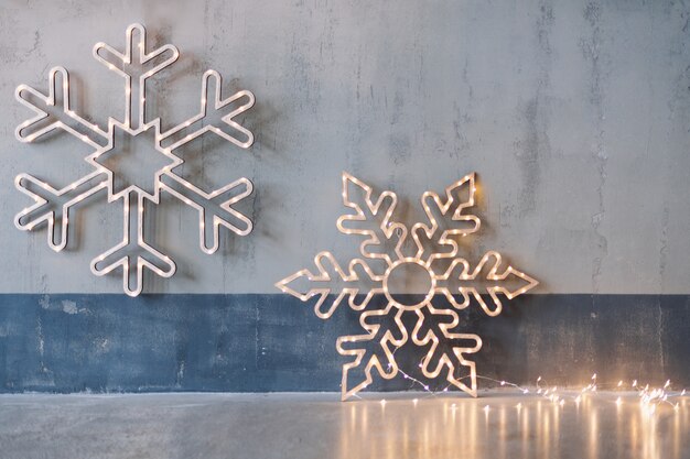 Decorazioni natalizie in legno per pareti. Fiocchi di neve incandescente con ghirlanda di luci su sfondo grigio cemento.