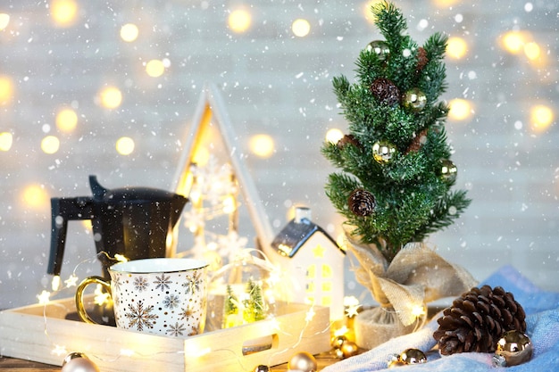 Decorazioni natalizie sul tavolo con una tazza e una caffettiera. Albero di Natale, vassoio - colazione mattutina di Capodanno con lucine e bicchieri.