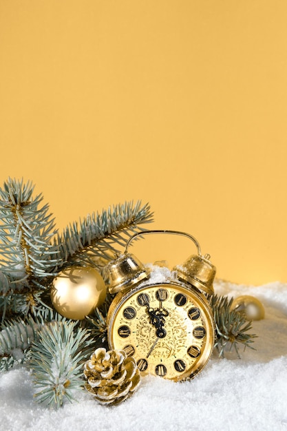 Decorazioni natalizie, sveglia in oro su sfondo giallo dorato. Sole, neve e ramoscelli di abete.