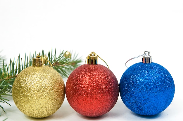 Decorazioni natalizie, tre palle di Natale rosso blu e giallo su uno sfondo bianco di close-up e un ramo di un albero di abete