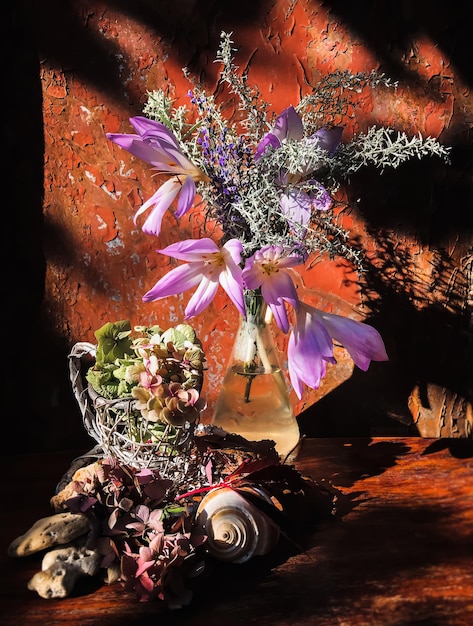 Decorazioni per la casa e composizione di fiori Bouquet autunnale in una fiaschetta di vetro con fiori di Colchicum fiori di ortensia secca conchiglia di mare e artemisia ai raggi del sole su un vecchio sfondo arrugginito