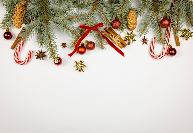Decorazioni per le vacanze di Capodanno o Natale Rami dell'albero di Natale palline rosse coni nastri rossi e fiocco bastoncini di cannella anice stelle e lecca-lecca su sfondo bianco Posto per il testo