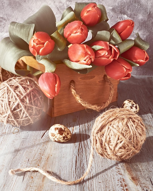 Decorazioni primaverili Decorazioni naturali a zero rifiuti Palline di canapa mazzo di tulipani rossi decorazioni primaverili e uova di Pasqua dipinte su tavolo di legno rustico grigio